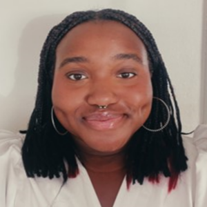 EMPH Student Alexa Osime stands indoors against a white wall, wearing a white top