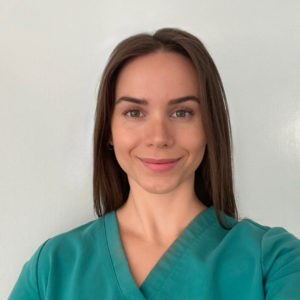 close-up photo of EMPH student Emily Brown wearing a green medical scrubs top, standing indoors against a white wall