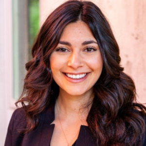 EMPH student Marina Martinez with a black blazer and brown shoulder length hair stands indoors