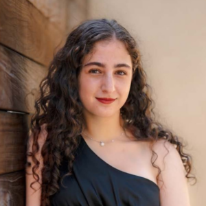 EMPH Student Sarah Hakakha stands against a wooden fence